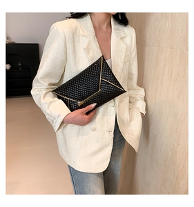 Close-up of black envelope clutch with woven texture and V-shaped gold metal trim