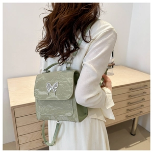 Detail of light green backpack with silver butterfly ornament and wrinkled patent leather texture