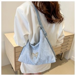 Detail of light blue wrinkled fabric shoulder bag with silver butterfly metal ornament