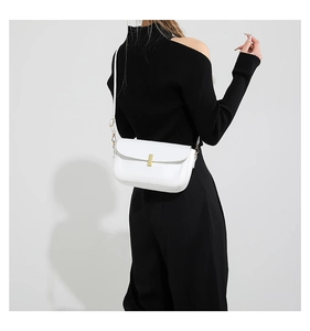 Detail view of a white minimalist shoulder bag with a gold metal lock on a black outfit