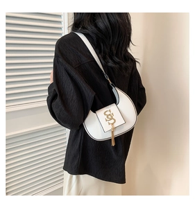 Detailed back view of white crescent bag with gold logo and tassel on a stylish model