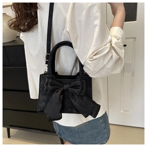 Detail of a black crossbody bag with a large decorative bow and adjustable strap