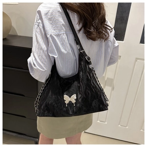 Détail d'un sac bandoulière en cuir noir avec un fermoir papillon en métal argenté