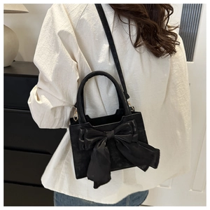 Fashionable black PU leather handbag with large bow detail worn as a crossbody bag