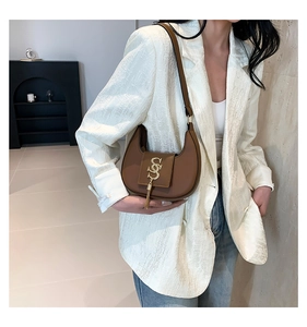 Close-up of brown crescent shoulder bag with gold logo detail and leather fringe tassel