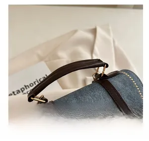 Detailed close-up of blue denim handbag with brown leather handles and gold stitching