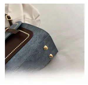 Detail of blue denim fabric backpack with brown leather trim and gold protective base studs