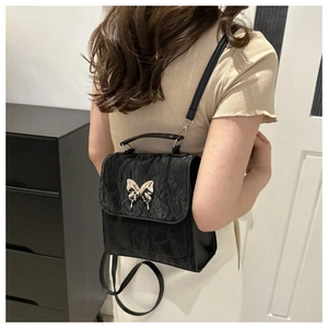 Close-up of a black textured backpack featuring a polished silver butterfly buckle detail