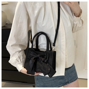 Chic black mini crossbody bag featuring a large satin bow and sleek leather-like finish