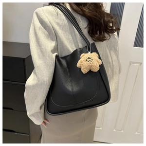 Détail d'un sac cabas en cuir noir avec accessoire charm ours en peluche marron