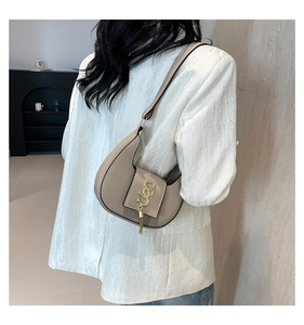 Detail of beige half-moon shoulder bag with golden geometric buckle and tassel charm