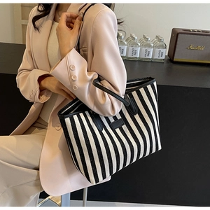 Sac cabas chic à rayures verticales et anses en cuir noir porté par un mannequin en costume