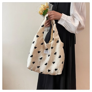 Detail of fabric tote bag featuring black heart patterns and a fashion brand label