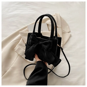 Detail of a black matte crossbody bag featuring a large soft bow and slender top handle