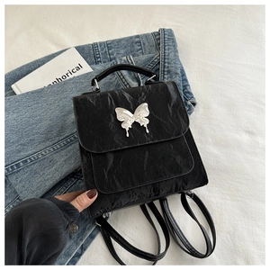 Détail du mini sac à dos noir texturé avec boucle papillon argentée et aspect froissé