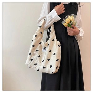 Detail of cream-colored tote bag featuring heart patterns and white fashion label tag