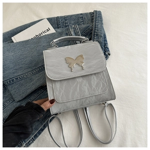 Gros plan du mini sac à dos argenté froissé avec un fermoir décoratif en forme de papillon