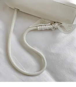 Détail du sac beige minimaliste montrant la bandoulière lisse et le nœud en foulard de soie