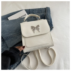 Vue détaillée d'un mini sac à dos blanc avec boucle papillon argentée sur tissu texturé