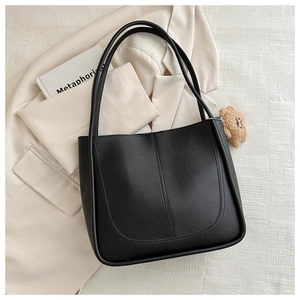 Détail d'un sac cabas en cuir noir avec surpiqûres en U et un pendentif ours mignon