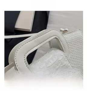Detail of white crocodile pattern leather handbag with square handle and fine stitching