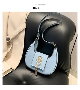 Detail of light blue crescent bag with gold logo and tassel on black leather sofa