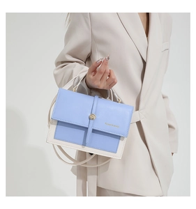 Detail of light blue and cream contrast stitching flap bag with metal buckle and top handle
