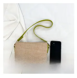 Detail shot of straw and green leather contrast bag with metal buckle and phone for scale