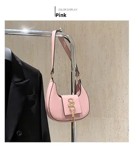 Detailed view of pink crescent bag featuring a gold S-shaped logo and long fringe tassel
