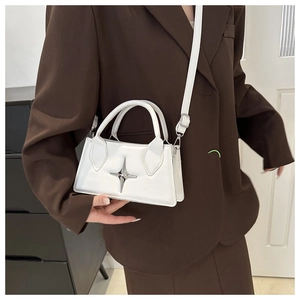 Dettaglio della mini borsa bianca con logo a stella in metallo indossata su un abito marrone
