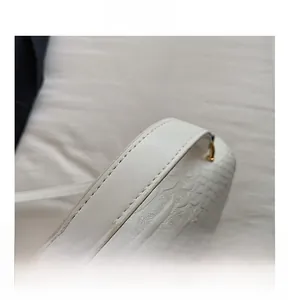 Detail shot of white crocodile embossed leather handbag with golden hardware and stitching