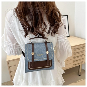 Close-up of a blue denim backpack with brown leather trim worn by a model in a cozy room