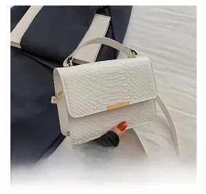 Detail shot of white faux crocodile leather texture and minimalist gold buckle on small square bag