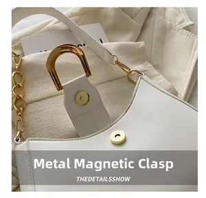 Detailed macro view of the gold magnetic hardware buckle on the white leather handbag