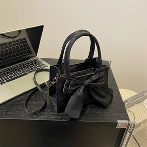 Minimalist black large bow tote bag with detachable strap on a modern desk setting