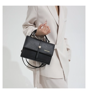Detail view of a black matte leather handbag with gold twist lock and brand logo