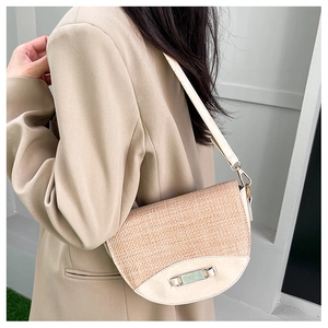 Detail of woven straw and beige leather saddle bag with silver buckle worn by model