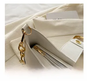Close-up of smooth metal zipper and golden chain hardware on white leather bag