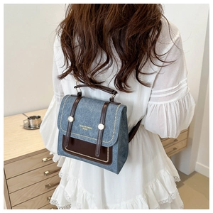 Detail showing the vintage denim blue backpack with brown leather flap and gold logo