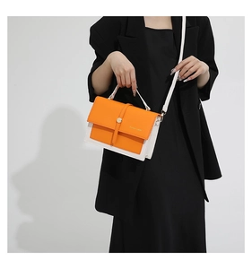 Détail du sac à main bicolore orange et blanc porté avec une robe noire élégante