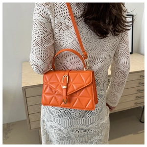 Detail of bright orange quilted crossbody bag with golden clasp worn by a model