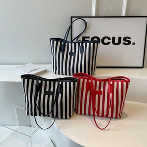 Three striped canvas tote bags with leather handles in navy, black, and red colors
