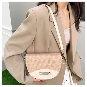 Detail of a straw crossbody saddle bag with contrasting leather trim and metal buckle
