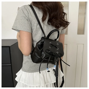 Close-up of black backpack with ribbon bow, criss-cross laces and beaded drawstring detail