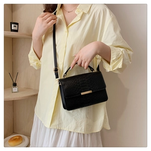 Detail of black croc-embossed handbag with gold clasp worn with elegant casual outfit