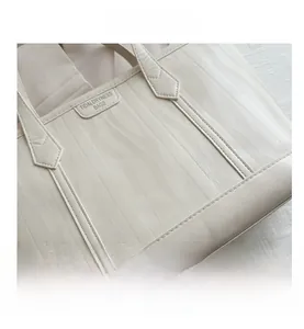 Detailed close-up of wavy embossed texture and stitched handle on beige tote bag