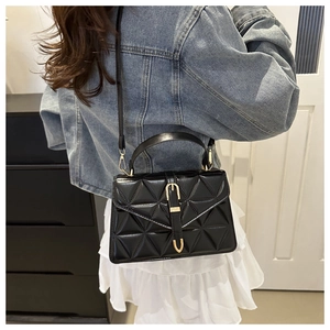 Close-up of black quilted shoulder bag with gold clasp and adjustable strap worn by model