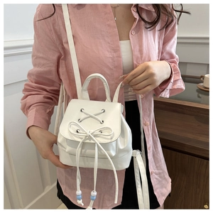 Detail of white mini bow backpack featuring a metal eyelet flap and slim straps