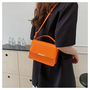 Close-up of bright orange crocodile-textured handbag with golden bar and shoulder strap