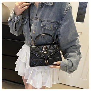 Close-up of black quilted crossbody bag with gold buckle on denim jacket and white skirt